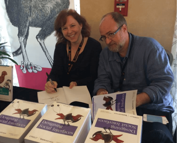 Picture of Christian sitting behind a table at a book signing, next to his co-author.